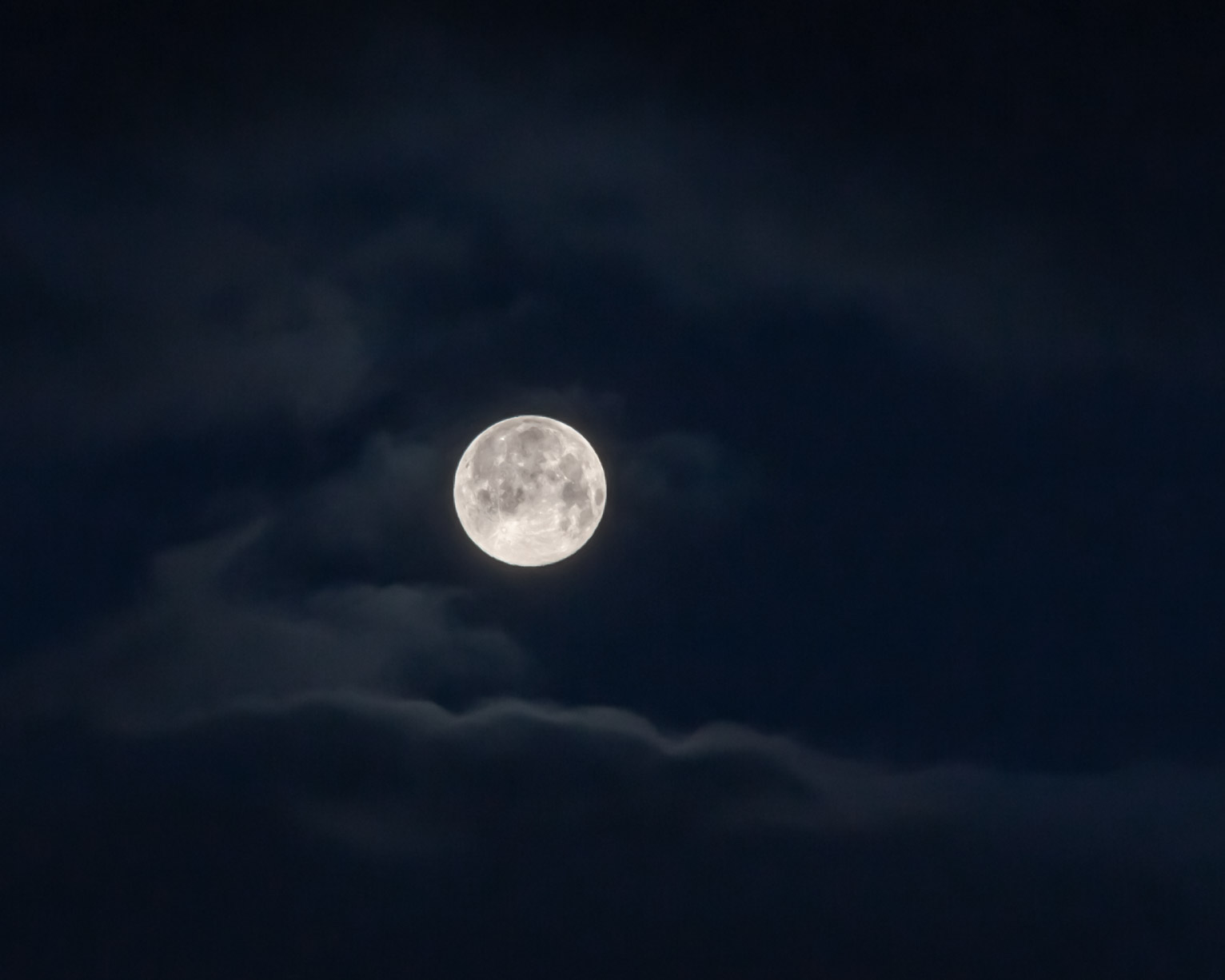 The full moon in a twilight sky lighting whispy clouds at early dawn